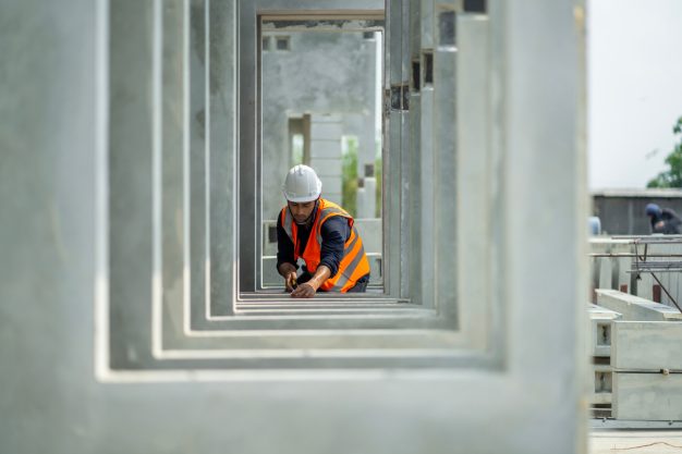 Trabajador con casco y chaleco naranja midiendo en una construcción. Estructura de hormigón.